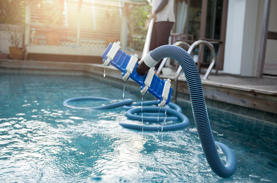 Technicien nettoyant une piscine creusée avec un aspirateur pour enlever les saletés au fond lors de l’ouverture
