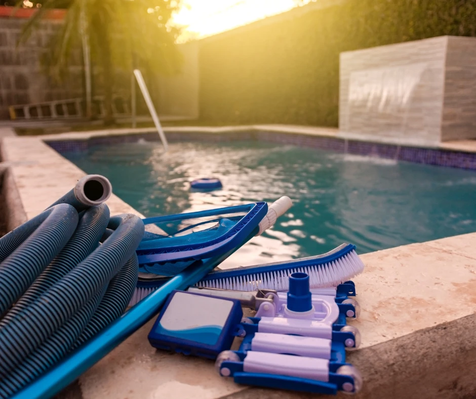 Piscine creusée moderne avec équipement d’entretien, comprenant un aspirateur de piscine, un skimmer et un tuyau de nettoyage sur le bord.
